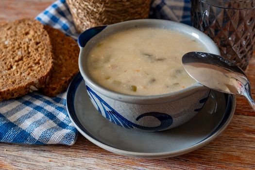 Warm soup in a stylish bowl with slices of wholegrain bread on a rustic table. Perfect for cozy dining.